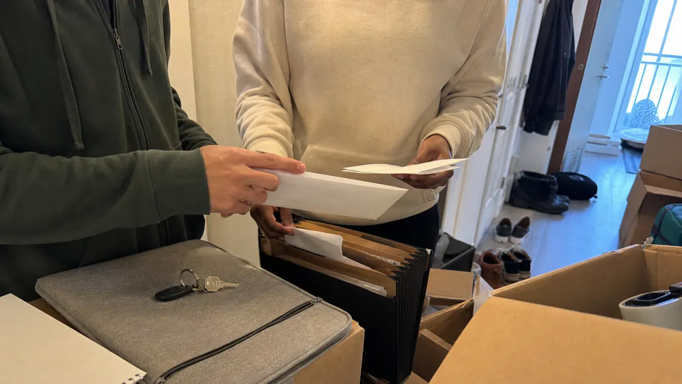 Partners sorting financial records into a folder among moving boxes in their apartment