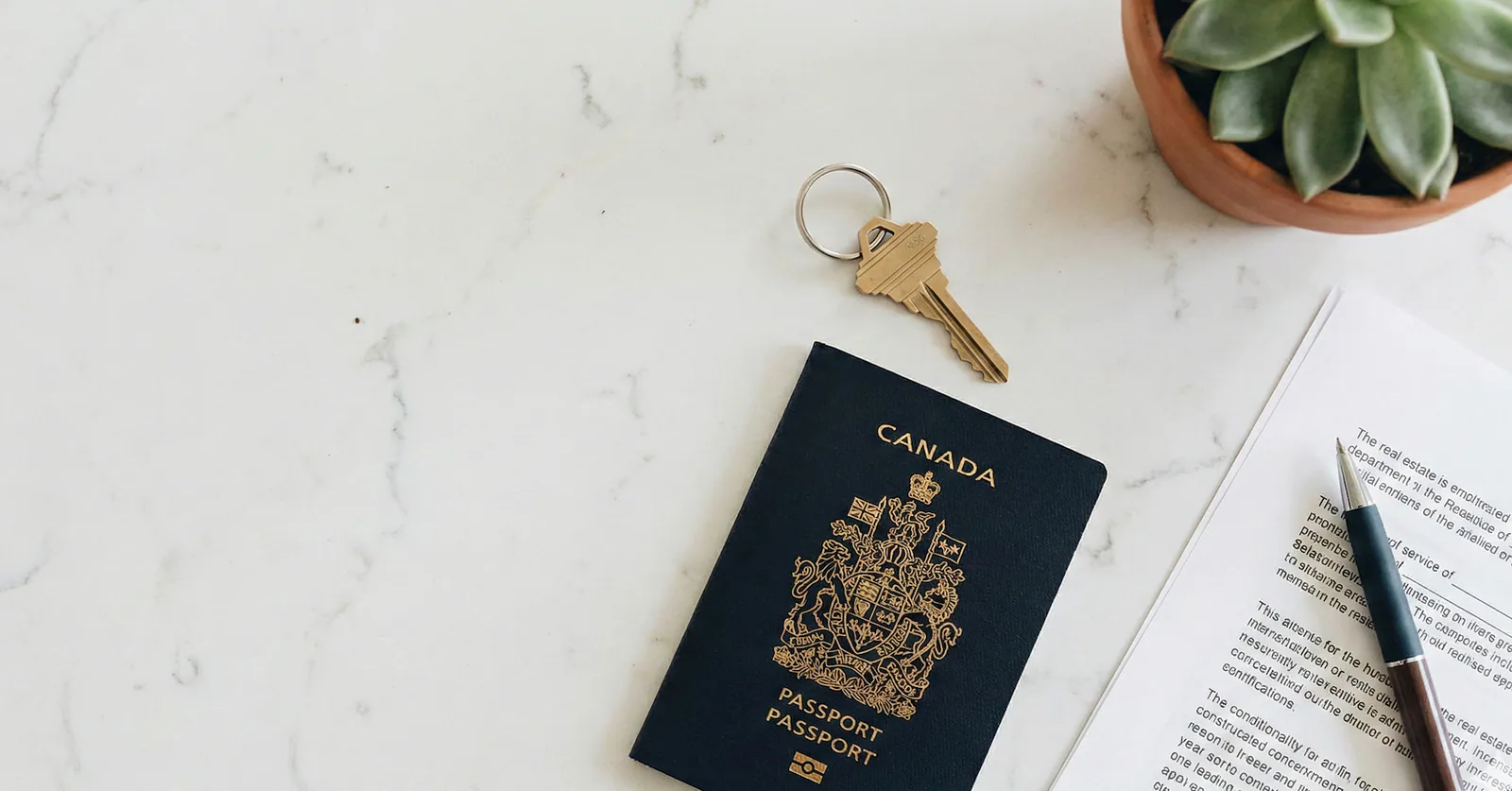 Canadian passport, house key, pen, paperwork, and a small plant on a marble desk